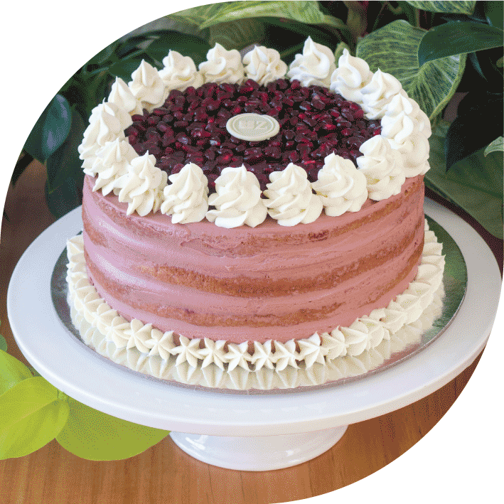 a purple and white pomegranate cake decorated with whipped white chocolate ganache and glazed poppy seeds