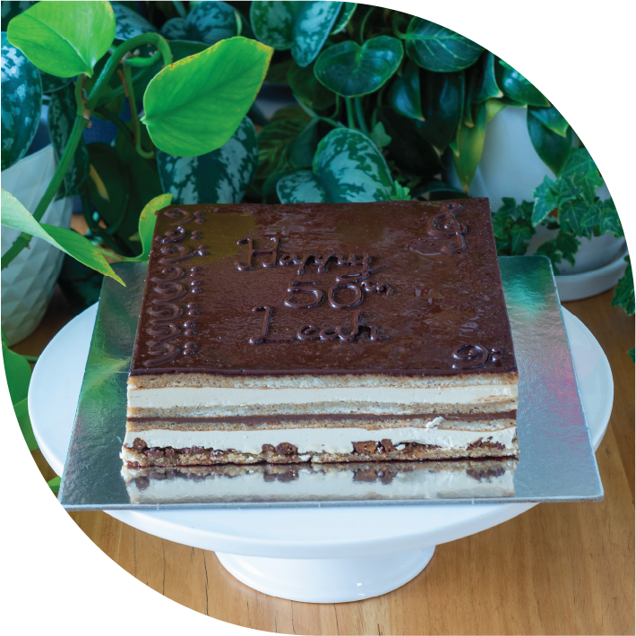A opera cake with visible layers of sponge, coffee buttercream and chocolate ganache with 'happy birthday' written on top