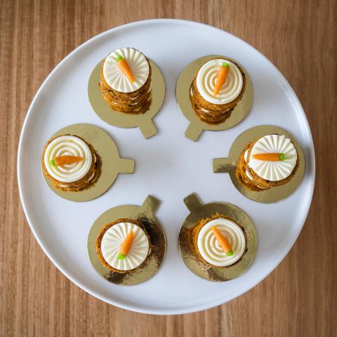 A set of six petit gateau carrot cakes seen from above with cream cheese icing and mini marzipan carrot decoration visible