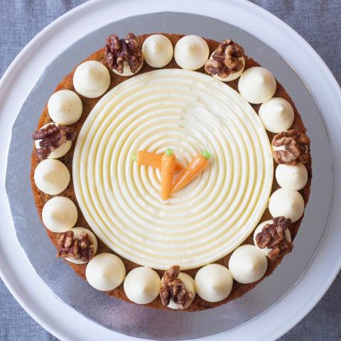 A carrot cake seen from above with cream cheese icing, caramalised walnuts and mini marizpan carrot decoration