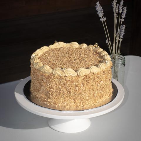 A mocha cake covered in caramelised almonds on a white cake stand in front of a vase with lavender