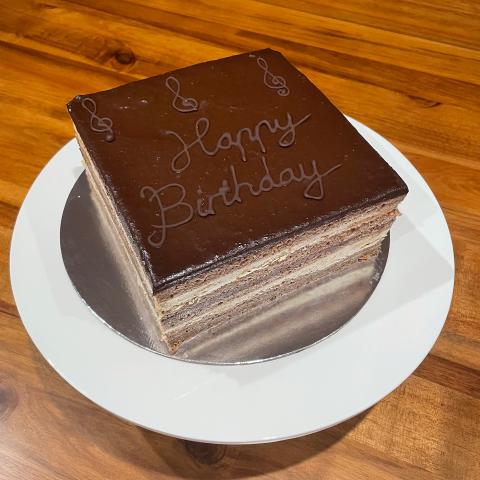 A opera cake with visible layers of sponge, coffee buttercream and chocolate ganache with 'happy birthday' written on top