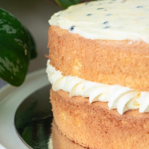 A close up of a passionfruit sponge with generous lashings of cream in the middle and passionfruit icing with visible passionfruit seeds on top