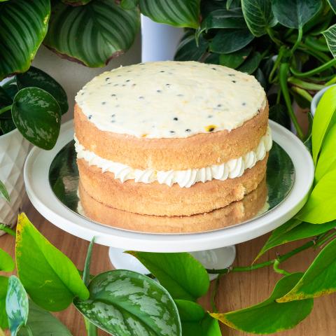 A passionfruit sponge on a white cake stand surrounded by plants