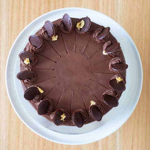 A prinzregententorte cake from above with chocolate buttercream rosettes, chocolate discs and gold leaf flakes