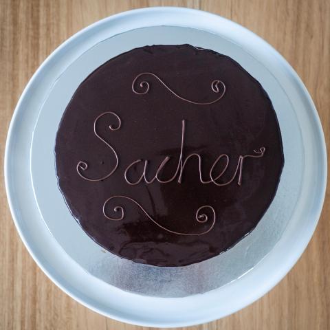 A glossy sachertorte on a white cake stand, seen from above.