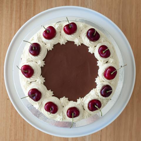 A black forest cherry cake seen from above on a white platter with cream rosettes, fresh cherries and chocolate ganache visible