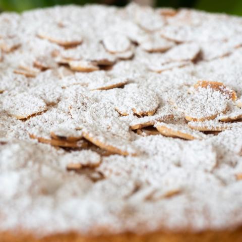 A close up of flaked almonds and icing sugar on top of a sponge cake