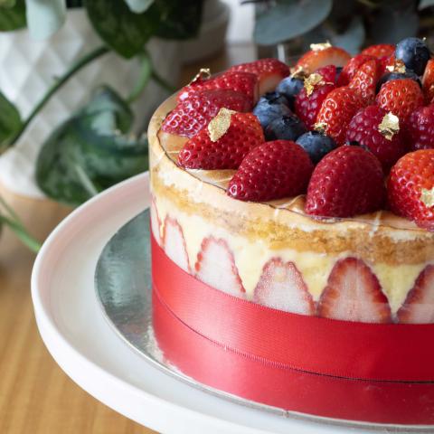A close up of a fraisier cake with visible strawberries, pastry cream and other berries on top on a white cake stand