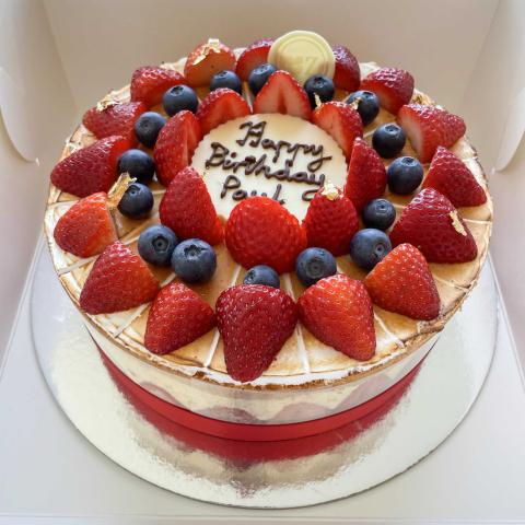 A fraisier cake with visible strawberries, pastry cream and other berries on top with a white chocolate plaque that says Happy Birthday