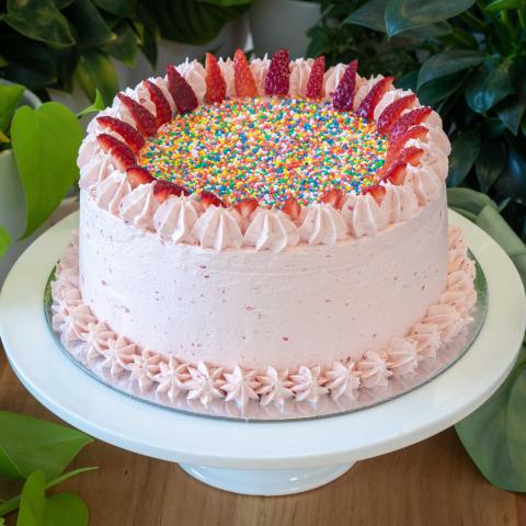 a pink strawberry cake decorated with 100s & 1000s and fresh strawberries