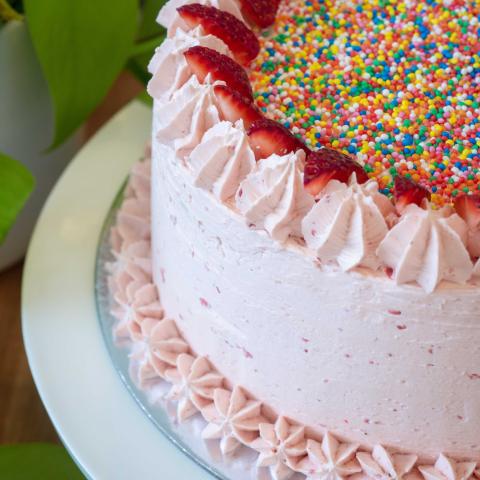 a close up of a pink strawberry cake decorated with 100s & 1000s and fresh strawberries
