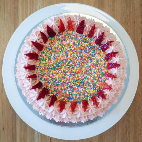 a pink strawberry cake decorated with 100s & 1000s and fresh strawberries viewed from above