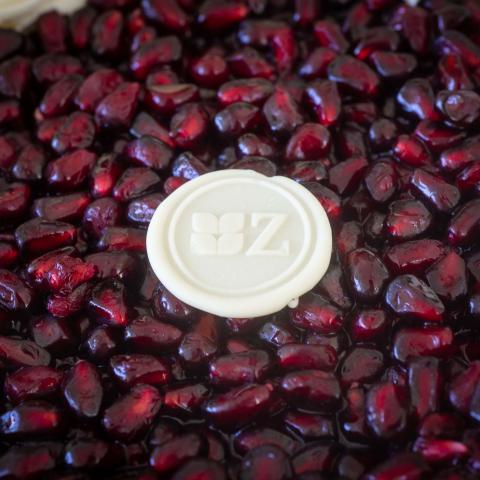 a close up of glazed pomegranate seeds and a white chocolate button with the Zuckerhaus logo stamped