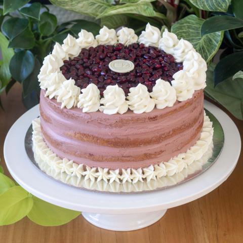 A pomegranate layer cake with pomegranate mousse and glazed pomegrante seeds with white chocolate whipped ganache pipping on a white cake stand