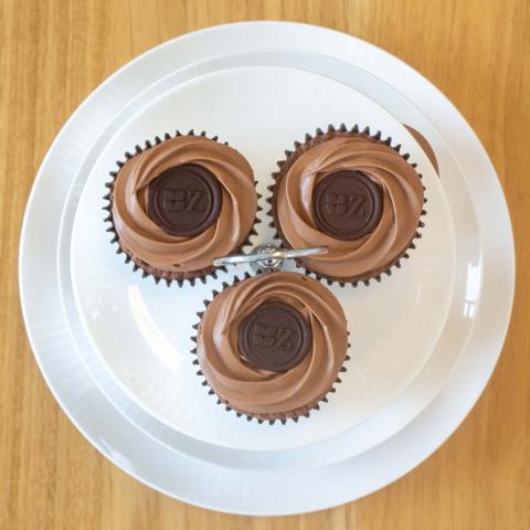 a top down view of three dark chocolate Sachertorte-inspired cupcakes decorated with dark chocolate buttons with Zuckerhaus logo on a white tiered high tea stand
