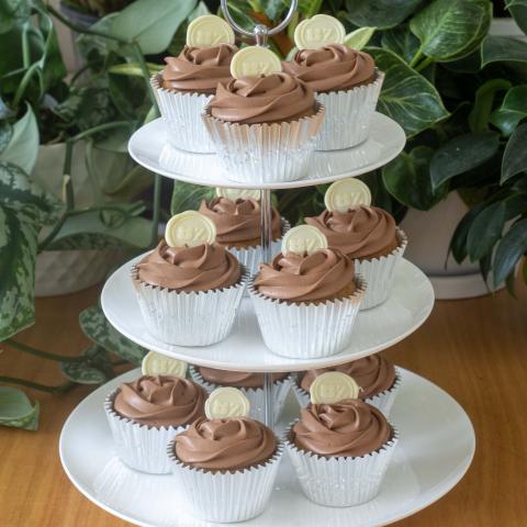 a white three tiered high tea stand with 12 chocolate iced Speculaas & Chocolate cupcakes decorated with white chocolate buttons with the Zuckerhaus logo