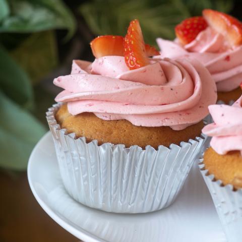 a close up of a pink strawberry cupcake decorated with fresh strawberries on top of pink buttercream