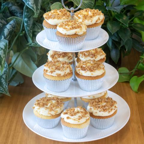 a white three tiered high tea stand with 12 golden Zitronen Sahne cupcakes decorated with white whipped ganache and golden toasted almonds