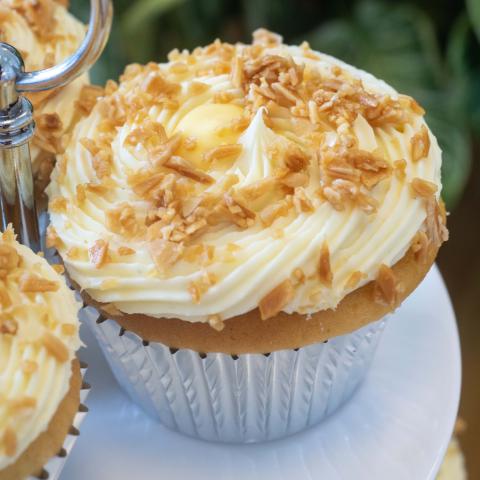 a close up of a Zitronen Sahne cupcake decorated with white whipped ganache, golden toasted almonds, and lemon curd centre