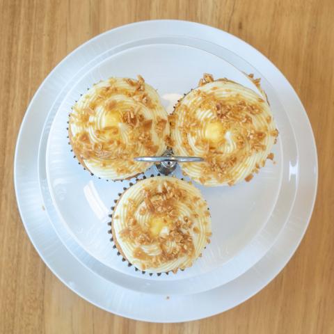 a top down view of three golden Zitronen Sahne cupcakes with white whipped ganache, toasted almonds and lemon curd centres visible