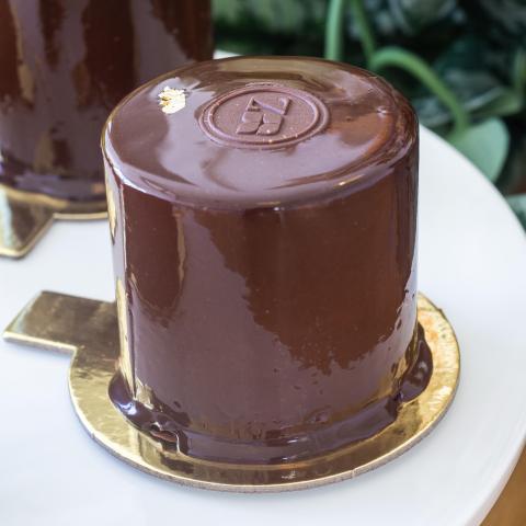 a glossy sachertorte petit gateau with chocolate Zuckerhaus button and gold leaf on top sitting on a white plate