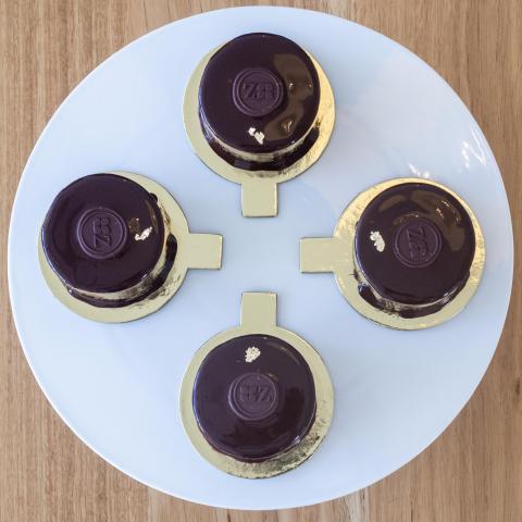 a top down view of four sachertorte petits gateaux on gold cake tabs sitting on a white plate