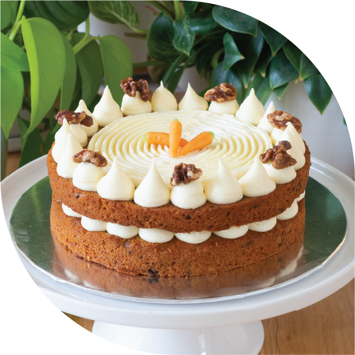 a two layered carrot cake with cream cheese between and on top decorated with mini marzipan carrots and caramalised walnuts