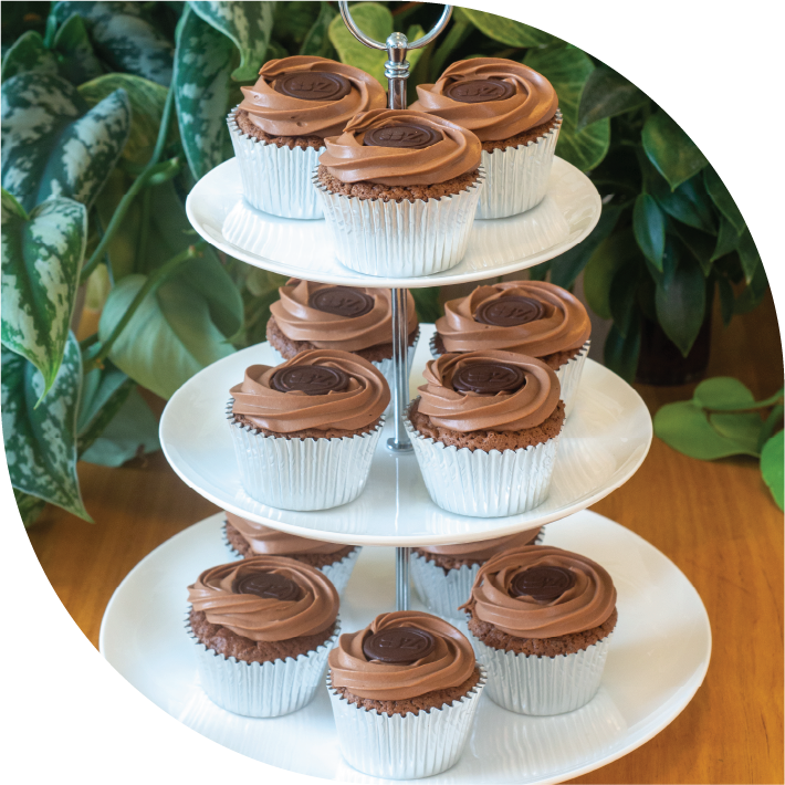a white three tiered high tea stand with 12 dark chocolate Sachertorte-inspired cupcakes decorated with dark chocolate buttons