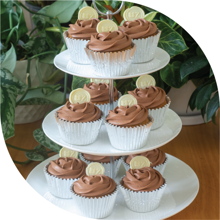 a white three tiered high tea stand with 12 chocolate iced Speculaas & Chocolate cupcakes decorated with white chocolate buttons with the Zuckerhaus logo