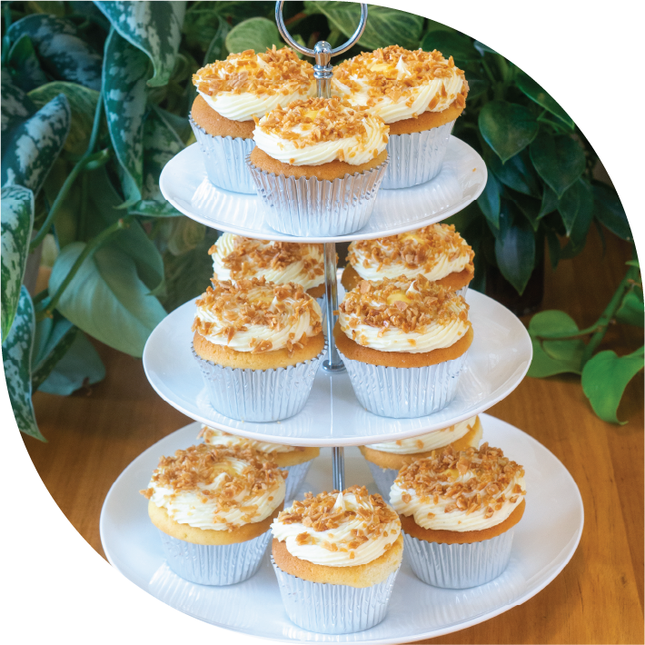 a white three tiered high tea stand with 12 golden Zitronen Sahne cupcakes decorated with white whipped ganache and golden toasted almonds